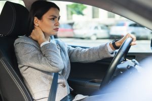 Woman in car holding neck in pain.